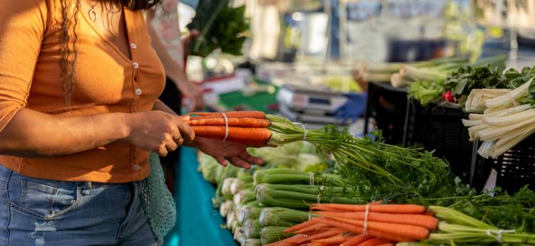 Young woman picks up carrots at farmers market.