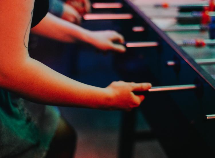 Two individuals are immersed in a competitive game of foosball at an arcade. Their focus is evident as they manipulate the rods to control the miniature soccer players, the game creating an atmosphere of intense concentration and fun in the dimly-lit venue.