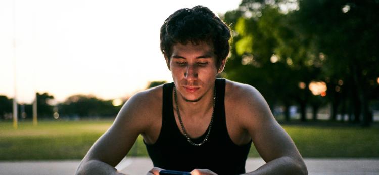 Young latino man at a basketball street court using his phone in the night