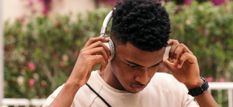 Young black man with afro hair, putting on white headphones to listen to music.