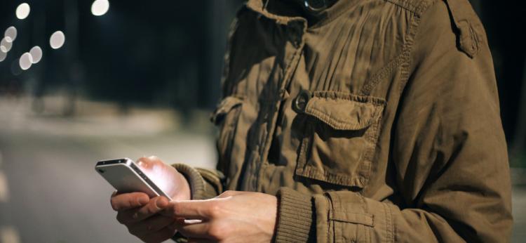 Young woman browsing on her mobile phone in the street during the night. Just hands and body 