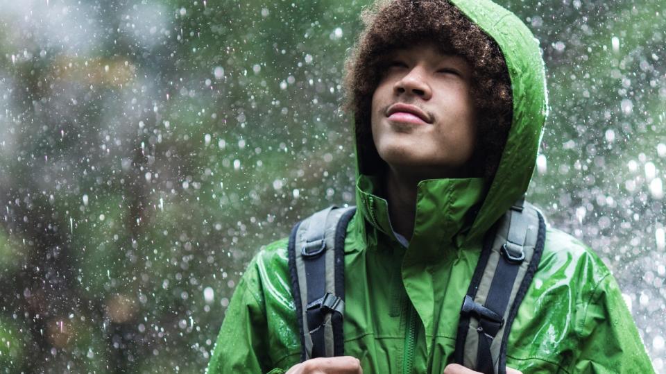 boy standing in rain wearing green raincoat