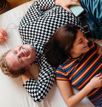 Homely scene of two young friends laughing together, one of them reading a book.